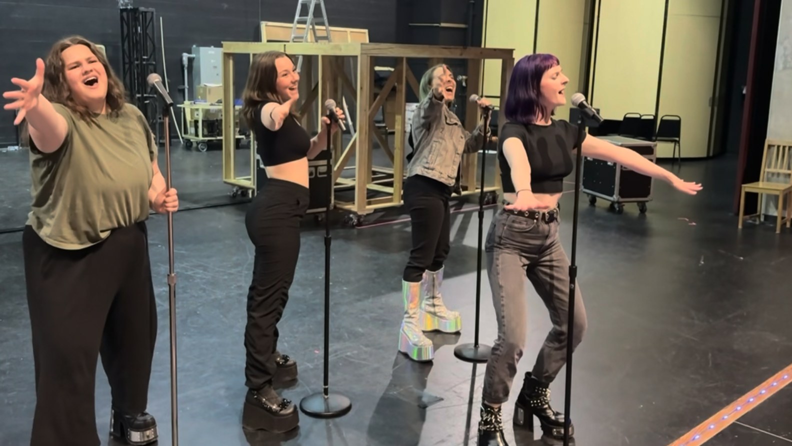 Four performers singing at microphone stands during a CLASS rehearsal